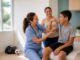 Nurse in blue scrubs examining a boy's bent arm as his mother and another woman look on and smile.